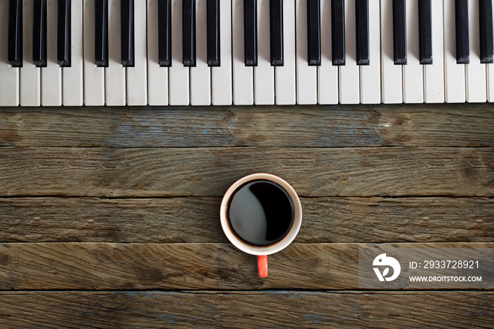 钢琴键和木制桌子上的红色咖啡杯，用于作曲家概念。
