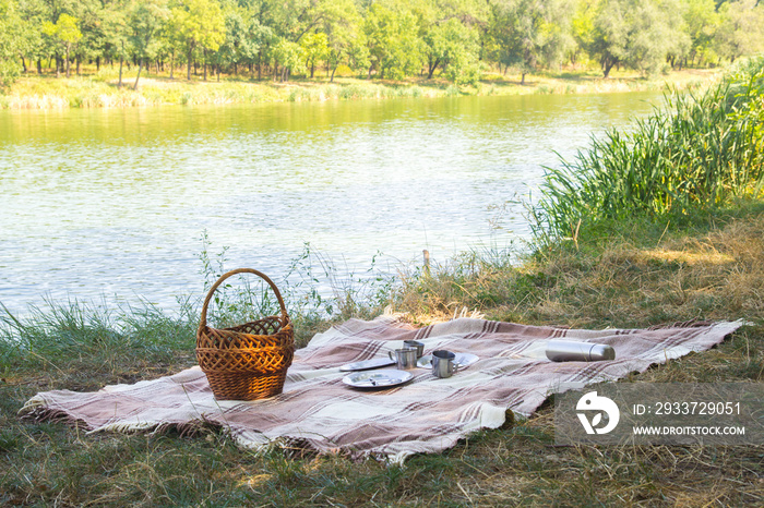 picnic set, metal Cutlery, thermos, plates tea cups. brown plaid and napkin from the lake in the bac
