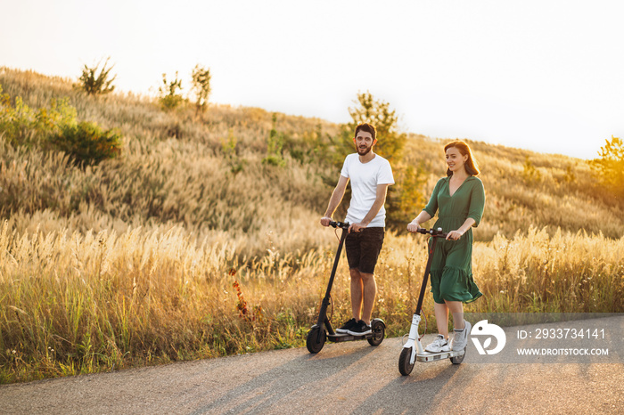 Young couple on vacation having fun driving electric scooter on the road in the countryside. Content