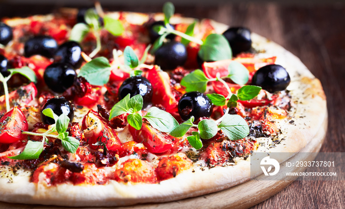 Pizza with cherry tomatoes, black olives and fresh oregano. Close up.