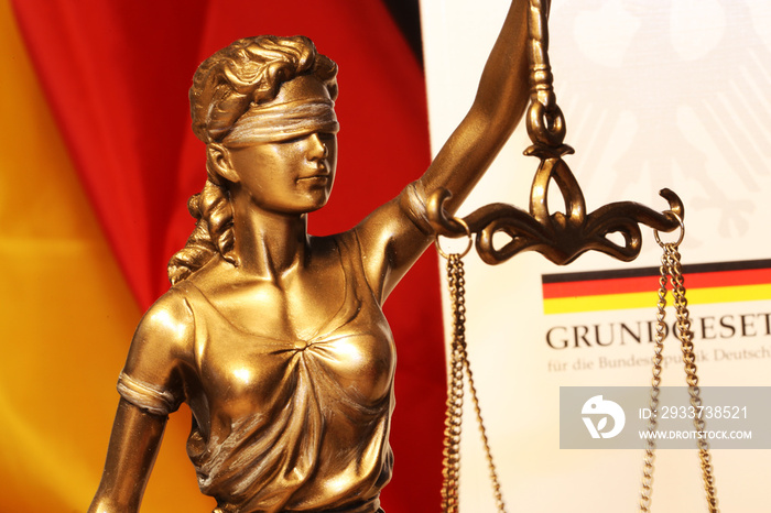 Nahaufnahme einer Justitia vor dem deutschen Grundgesetzbuch