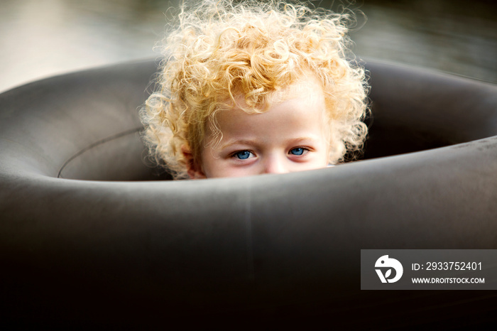 Portrait of blond girl hiding in tire