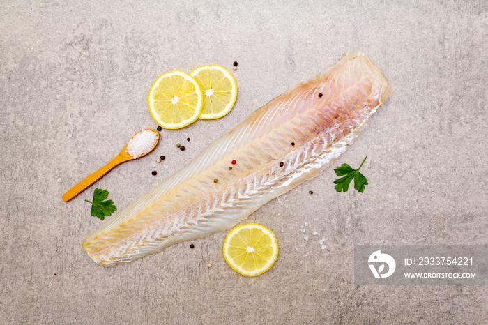 Fresh raw hake fillet on a stone background. With lemon, parsley, salt in wooden spoon and peppers m