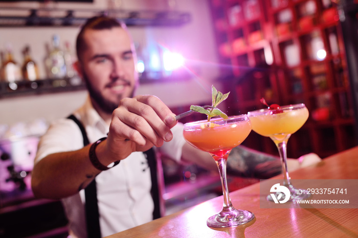 handsome bartender prepares an orange alcoholic cocktail and smiles on the background of a bar or a 