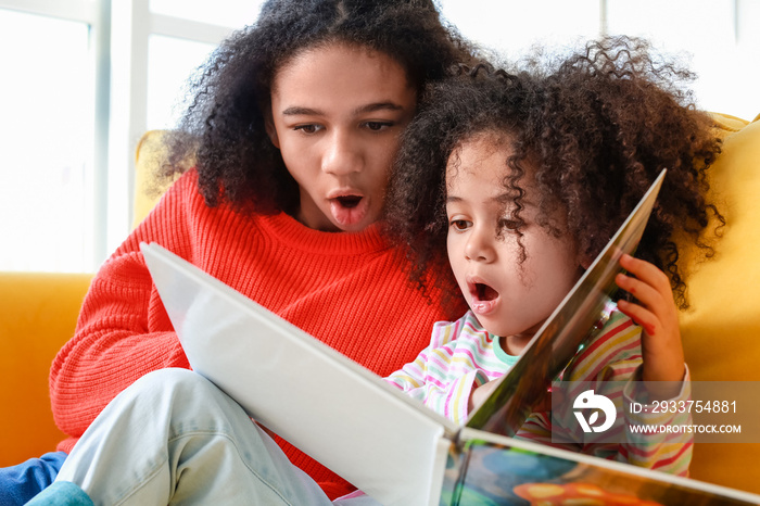 Cute African-American sisters reading book at home