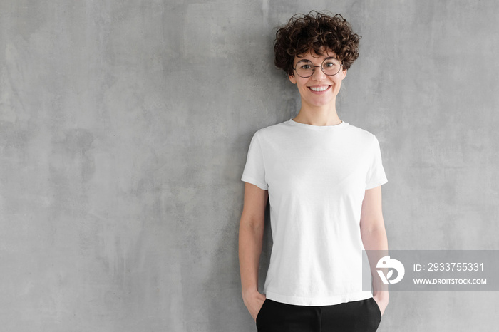 Hotizontal portrait of young woman wearing blank white t-shirt, posing against gray textured wall