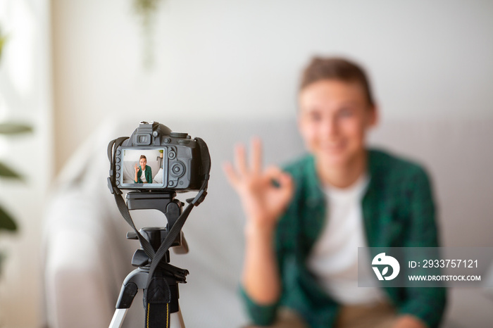 Selective focus on camera shooting teen guy showing okay