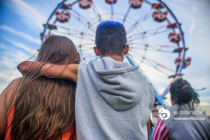 Rear view of teenage couple looking at ferris wheel in amusement park