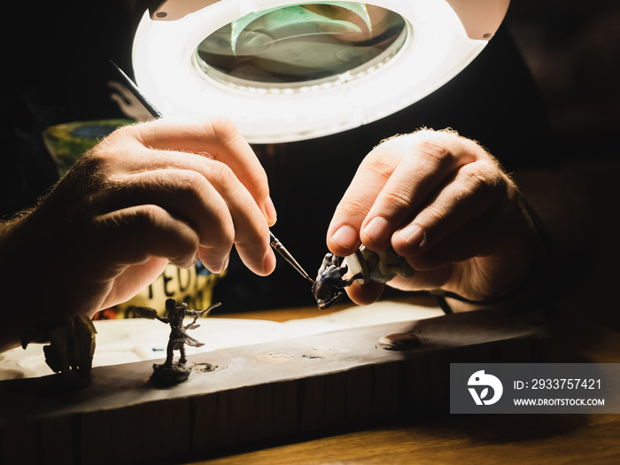 human hands painting under the lamp with light and magnifying glass plastic minifigures for board ga