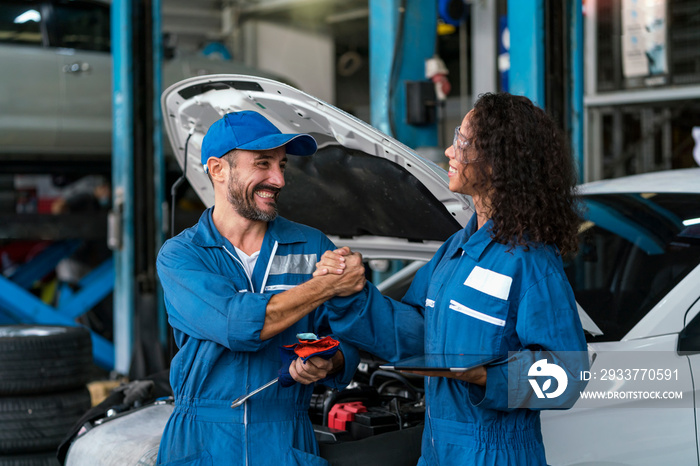 Two happy auto mechanics in uniforms working in auto service with car. Two men handshake mechanics i