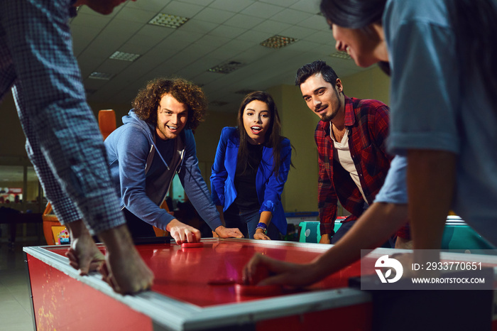 A group of friends playing air hockey in an amusement park.