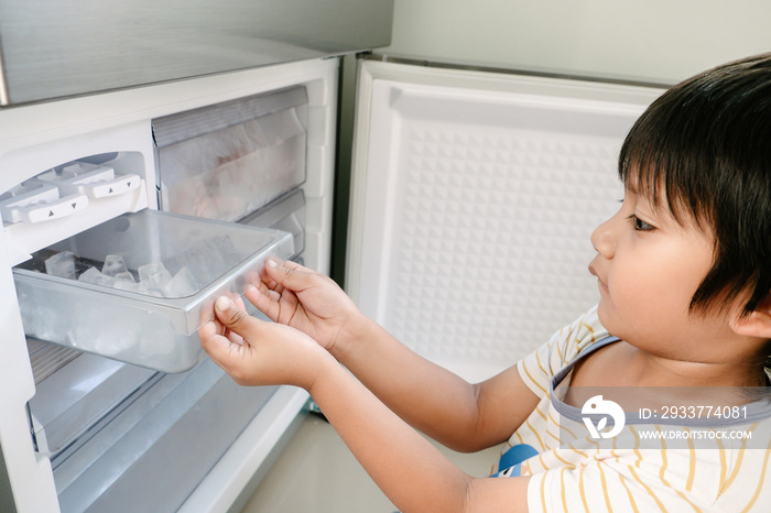 亚洲小孩用冰箱里的制冰机制冰