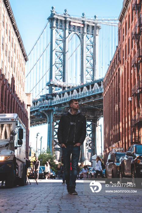 一个年轻人走在布鲁克林的华盛顿街上，背景是曼哈顿的一座桥。