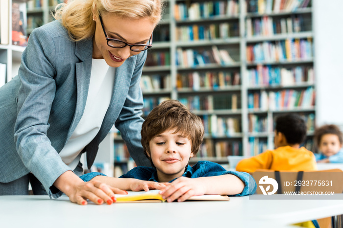 beautiful woman standing near cute child reading book