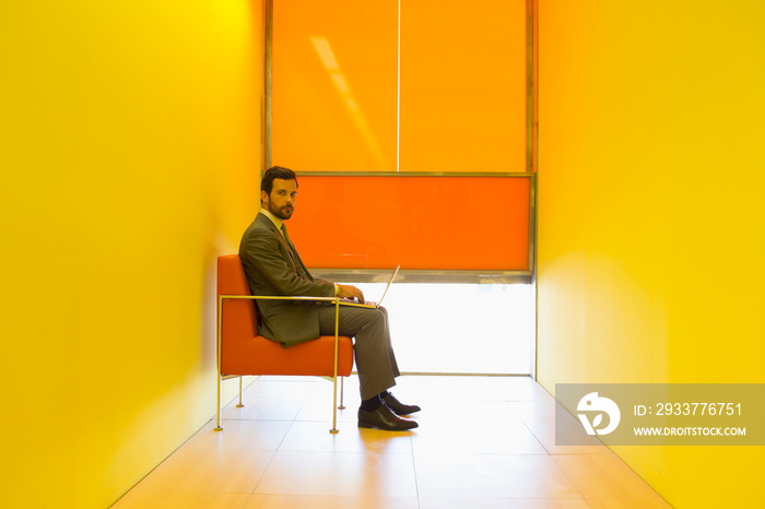 Portrait confident businessman using laptop in modern yellow office