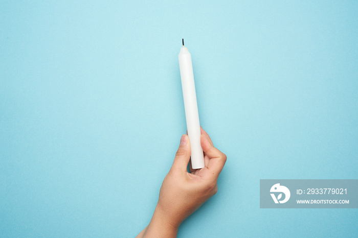 female hand holding a white wax candle on a blue background