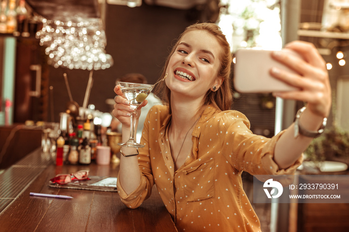 Glowing lady taking selfies while being at the bar with a drink.