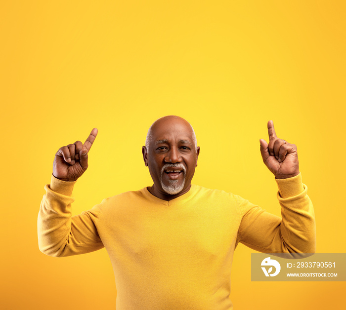 Elderly African American man pointing upwards at free space, recommending something, offering huge s