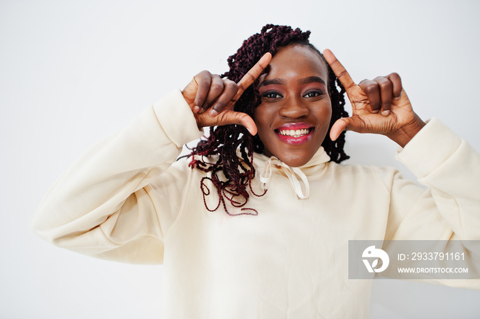 African woman in hoodie stand against white wall and show frame on head by fingers.