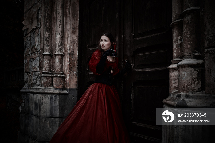 神秘女子身穿维多利亚时代红色连衣裙，手持蜡烛