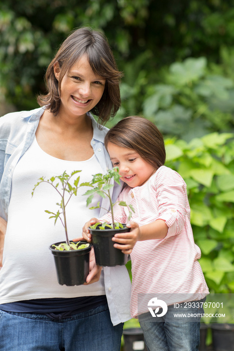 Portrait happy pregnant mother and daughter with saplings