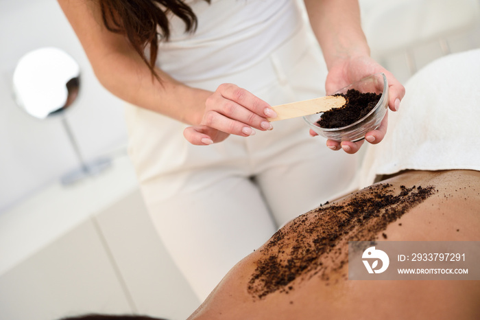 Woman cleans skin of the body with coffee scrub in spa wellness center.