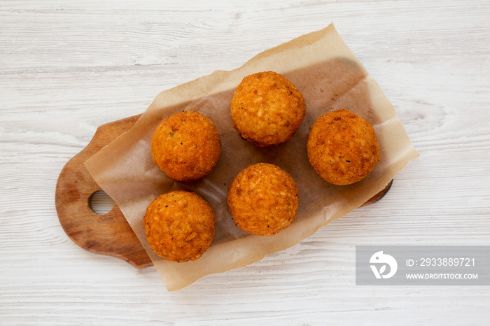 Homemade fried Arancini on a rustic wooden board on a white wooden surface, top view. Italian rice b