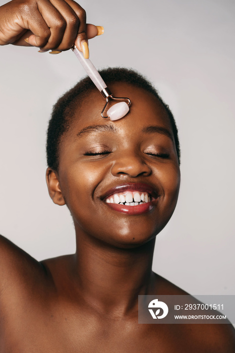 African american woman with closed eyes making face massage using jade roller, isolated on white bac