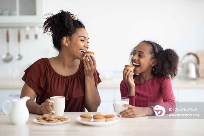 Pretty black mother and teen daughter eating cookies