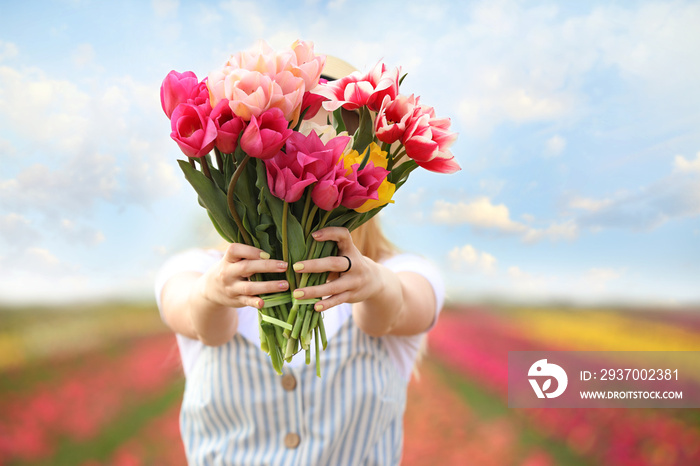 Beautiful young woman with bouquet of fresh tulips in countryside on spring day