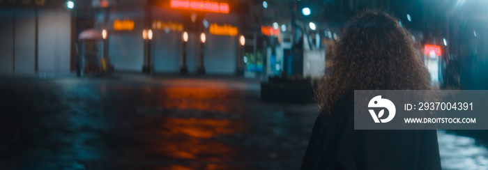 Curly hair woman in a white t-shirt and black jacket leaves a wonderful street with red led lights a