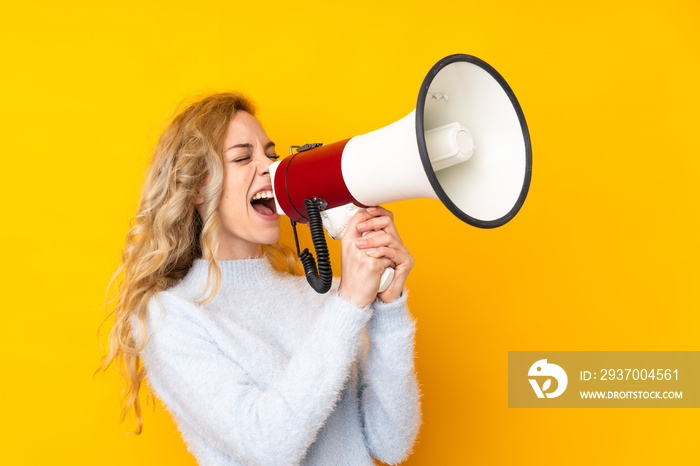 Young blonde woman isolated on yellow background shouting through a megaphone