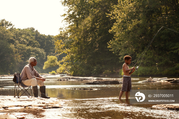 Grandfather looking at his grandson fishing in river