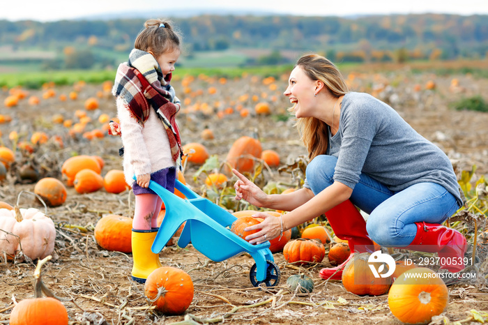 Little kid girl and beautiful mother having fun with farming on a pumpkin patch. Traditional family 