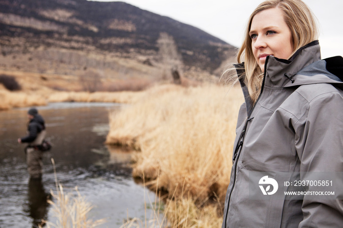 Woman by stream with man fishing