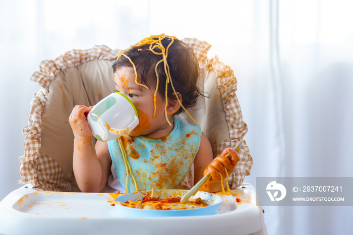 Adorable little toddler girl or infant baby drink water after eat delicious spaghetti food on chair.