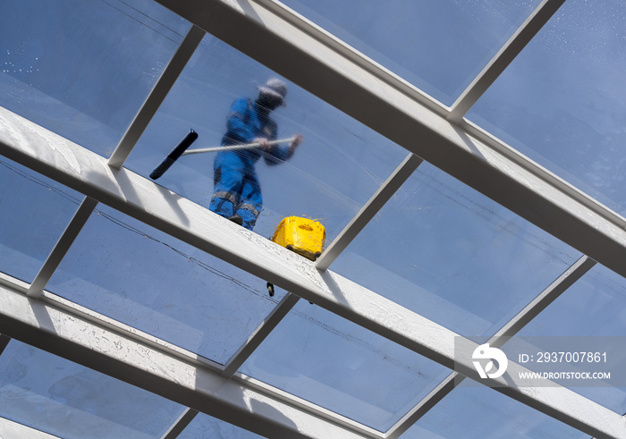 Male worker washing large expanse of glass roof over swimming pool