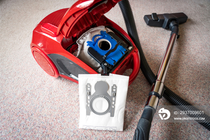 Inside A red vacum cleaner with old and new vacum filter bags laying on a white carpet floor. Cleani