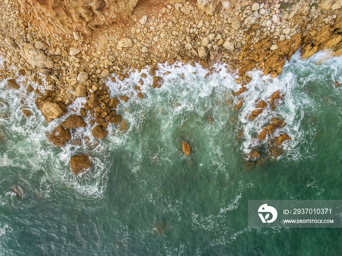 Aerial. Waves beat against the shore, the view from the sky.