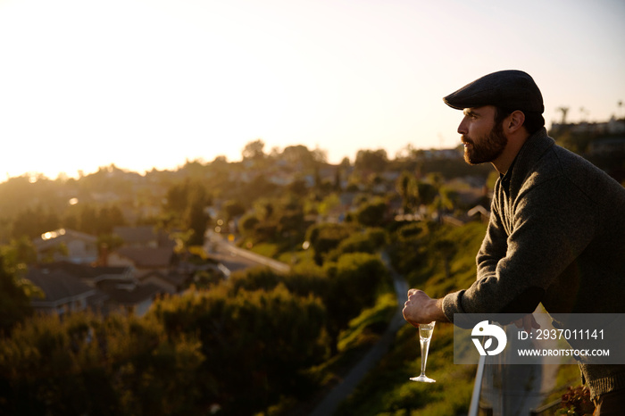 Man with wine glass leaning on railing and looking at view