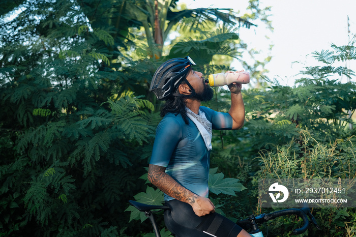 A young bearded cyclist drinking from a drinking bottle.