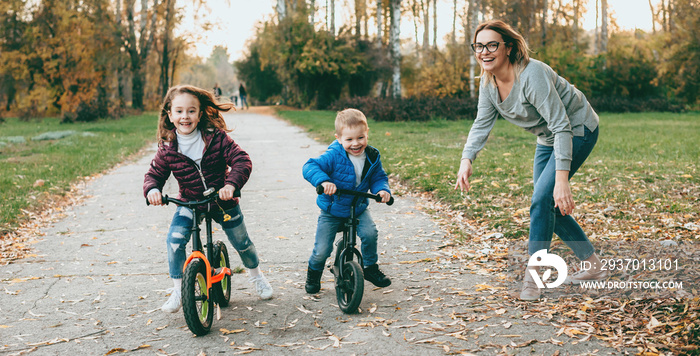 可爱的母亲和她的孩子们在公园里散步，教他们骑自行车