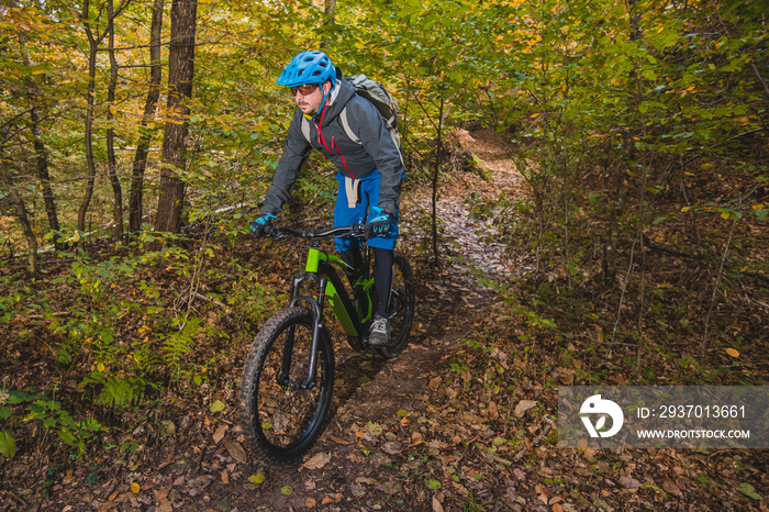 Biker riding downhill with a modern electric bicycle or mountain bike in autumn or winter setting in