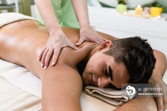 Good looking young man enjoying in massage in the spa salon.