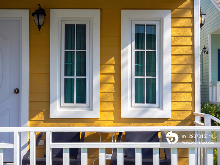 两扇白色的窗户，玻璃，绿色窗帘装饰在附近的黄色木制居民身上