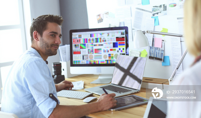 Portrait of young designer sitting at graphic studio in front of laptop and computer while working o