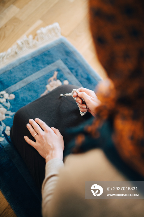 High angle view of woman praying with rosary beads on carpet at home