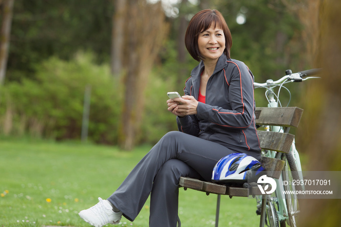 Pretty Asian woman texting on smartphone in the park