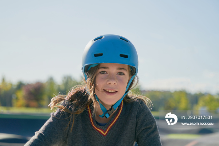 戴着蓝色安全自行车头盔，以城市景观和自然为背景的微笑女孩