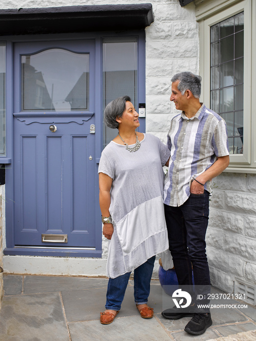 Smiling couple standing in front of house